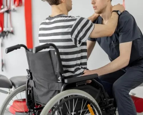 rehabilitation-specialist-helps-man-get-up-from-wheelchair-clinic-1.webp